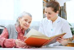 caregiver helping an elderly woman reading