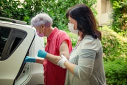 caregiver helps her elderly client to get into a car